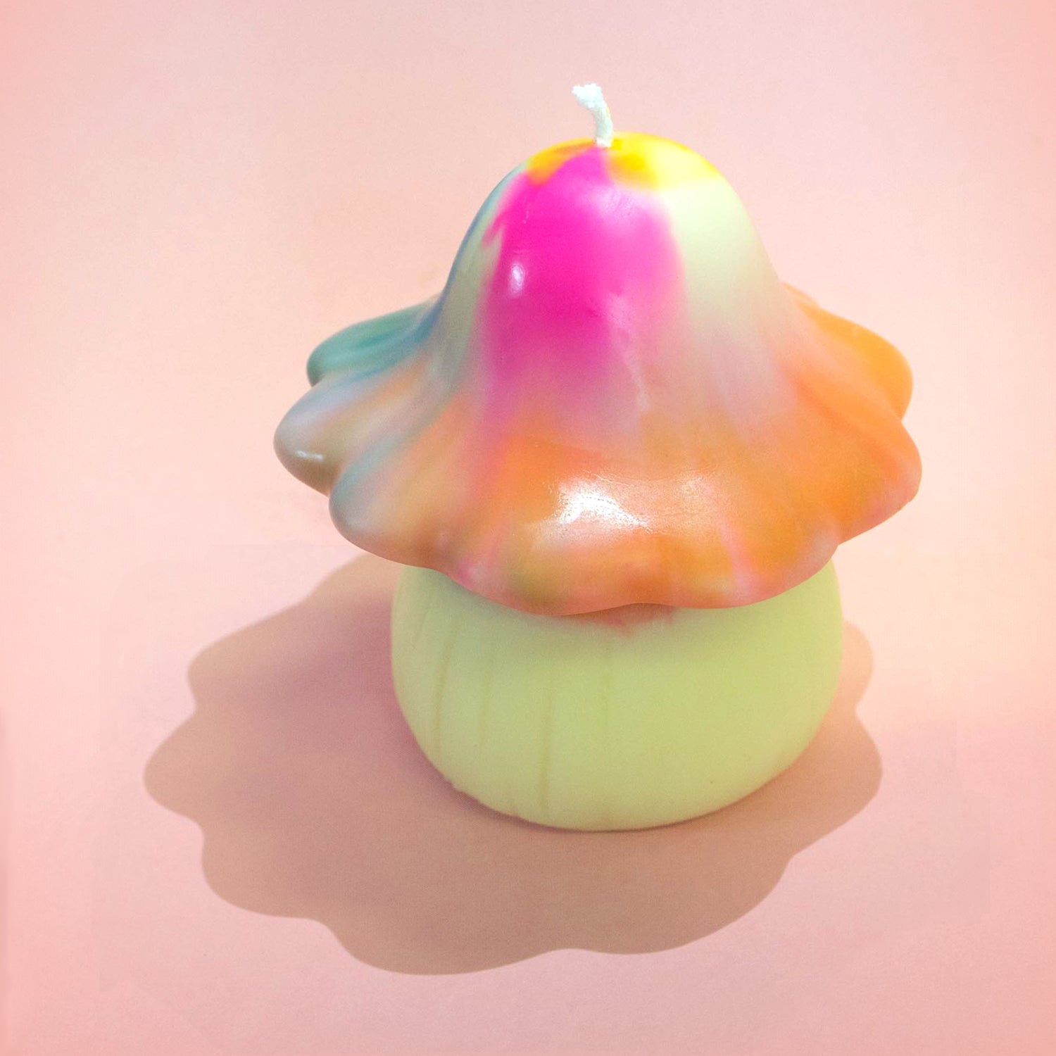 A scalloped edged mushroom candle. The head of the mushroom has a rainbow tie-dye effect. A whimsical, funky candle inspired by funghi.