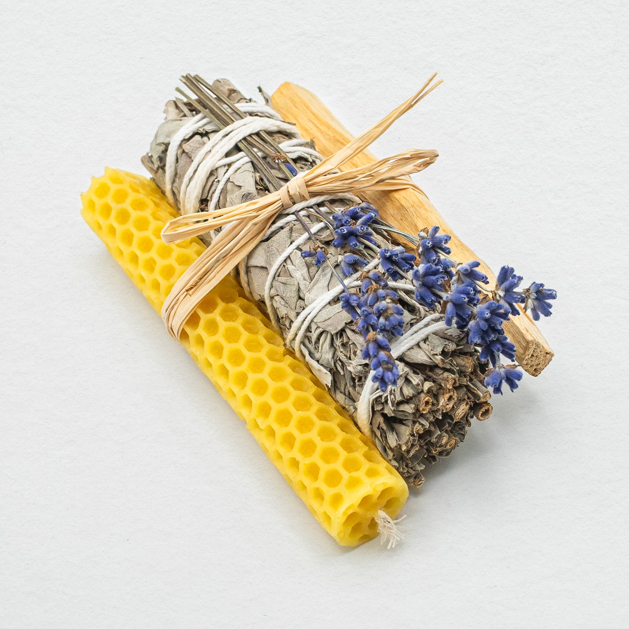 white sage bundle, with a honeycomb textured beeswax candle and a stick of palo santo, and a bunch of purply blue lavender. All tied together with a piece of raffia.